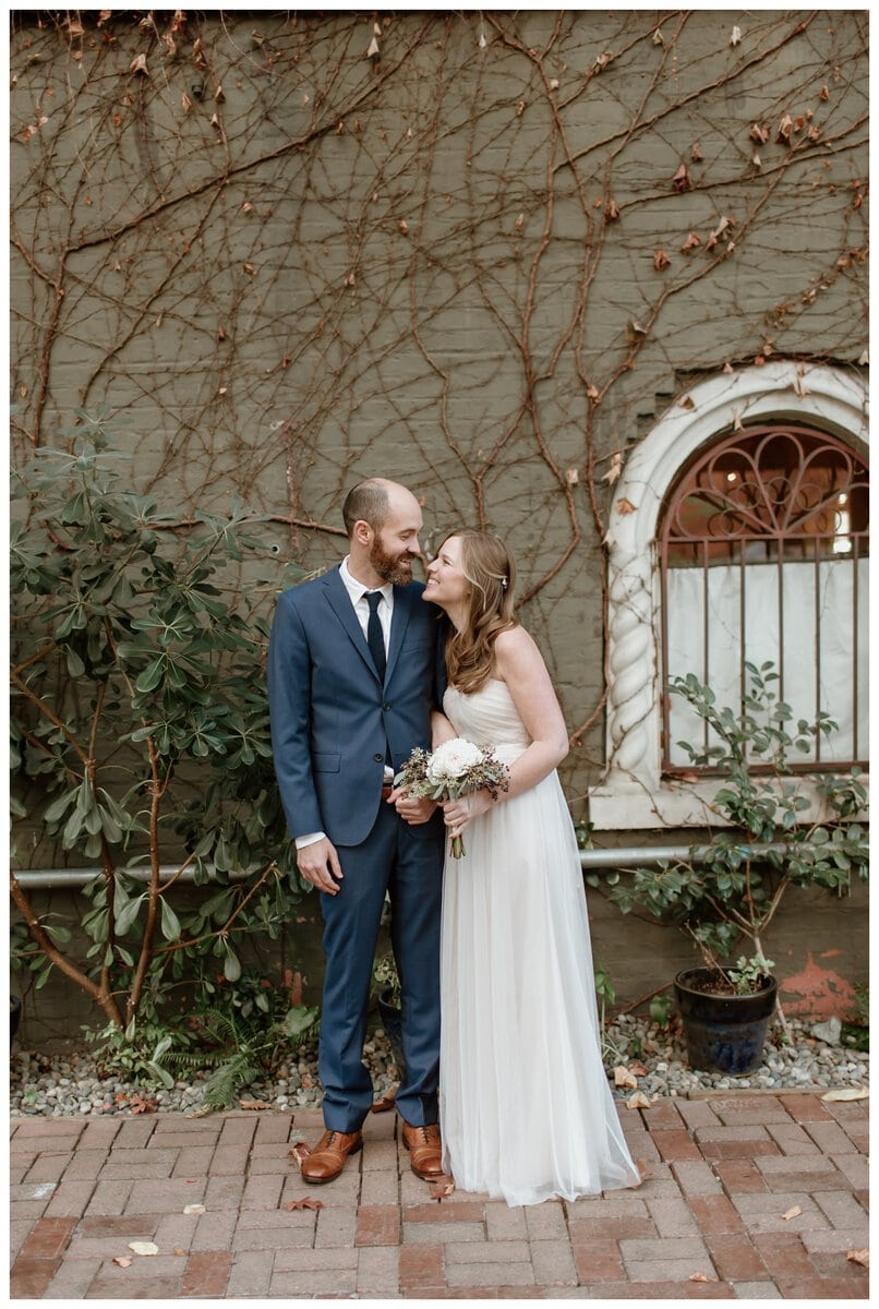 A joyful couple shares an intimate moment before their ceremony, surrounded by the charm of ivy-covered walls. Their loving connection makes couples ask, "Should we do a first look on our wedding day?"