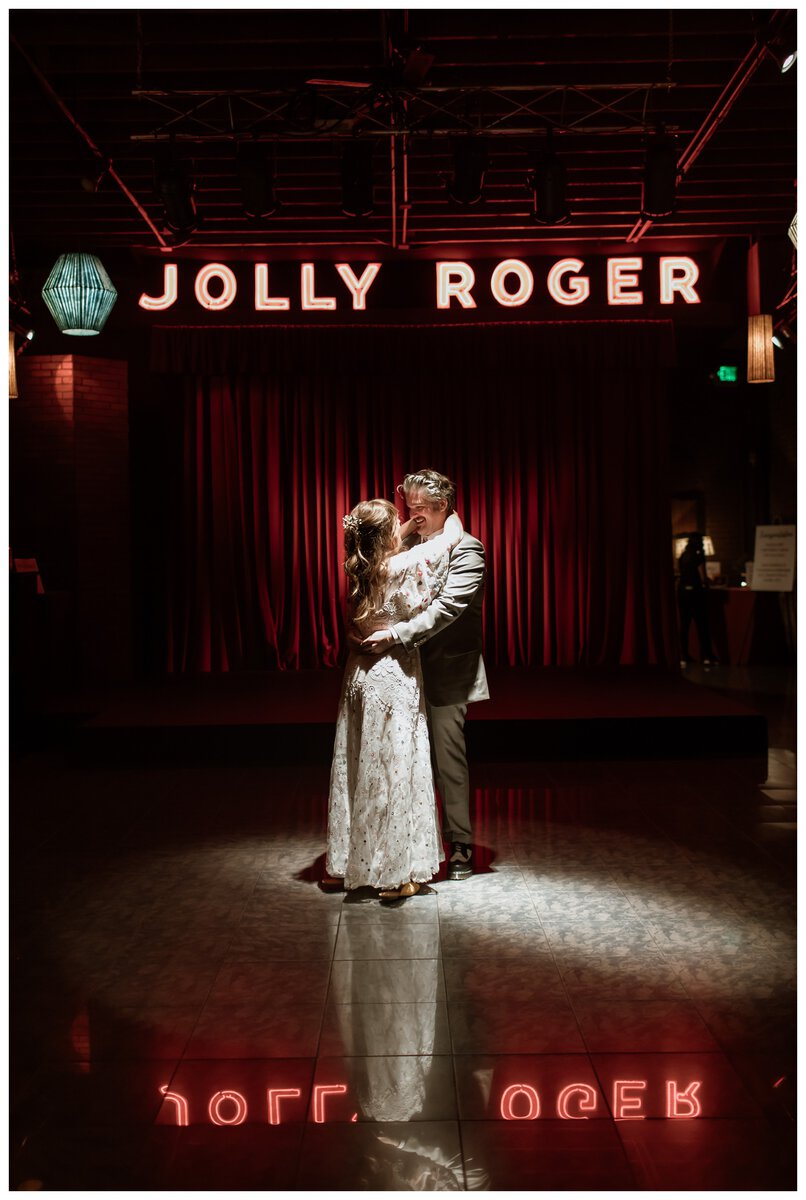 A bride and groom share a romantic first dance under moody red lighting at the Georgetown Ballroom. Their intimate moment perfectly captures the magic of choosing cool first dance songs for an unforgettable wedding celebration.