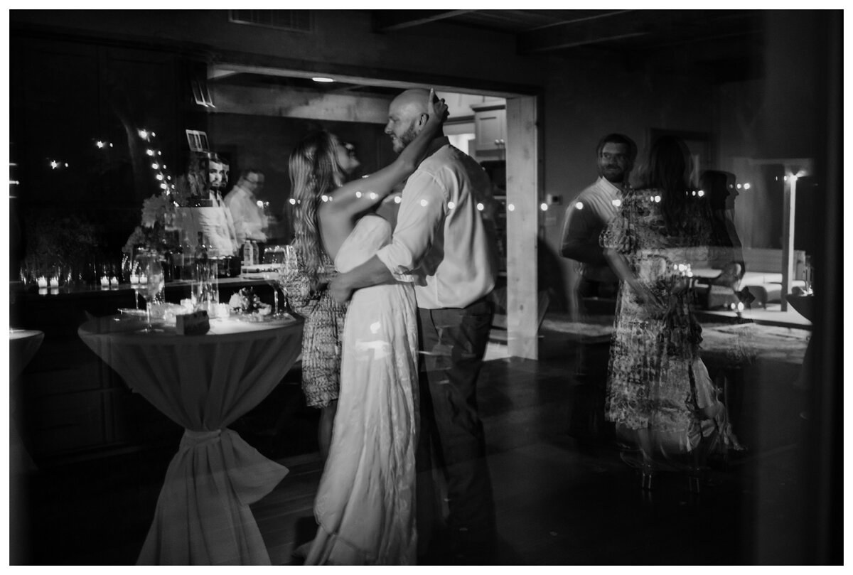 A romantic black-and-white moment captures a couple sharing their first dance, surrounded by warm reflections and candlelit ambiance. This intimate scene perfectly complements the magic of cool first dance songs that set the tone for an unforgettable wedding night.