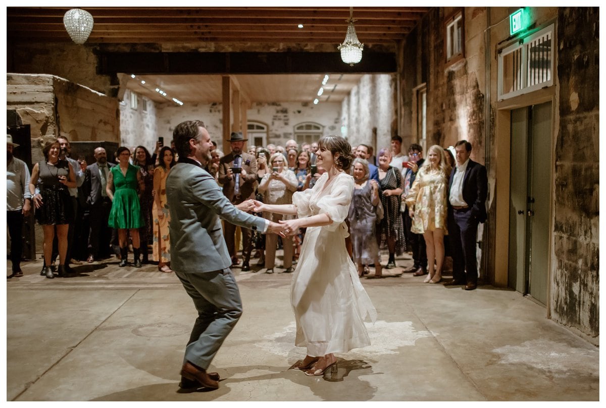 Bride and groom sharing their joyful first dance at the historic Ingenhuett on High venue, surrounded by family and friends. A beautiful moment captured in a rustic and elegant wedding setting.