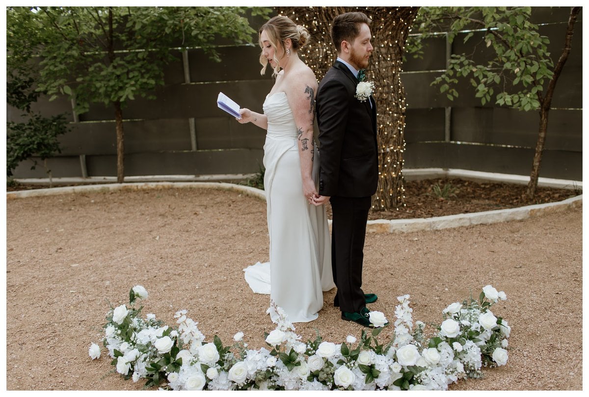 A heartfelt first touch moment at Artspace111 Fort Worth wedding, where the bride and groom stand back-to-back, holding hands and exchanging personal vows before their ceremony.