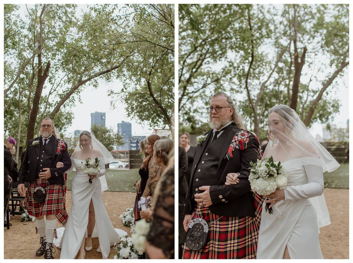 Bride walks down the aisle with her father at an Artspace111 Fort Worth wedding, surrounded by family and friends. The father wears a traditional Scottish kilt, while the bride stuns in an elegant off-the-shoulder wedding gown with a flowing veil. The outdoor ceremony space features lush greenery and a view of the Fort Worth skyline in the background.