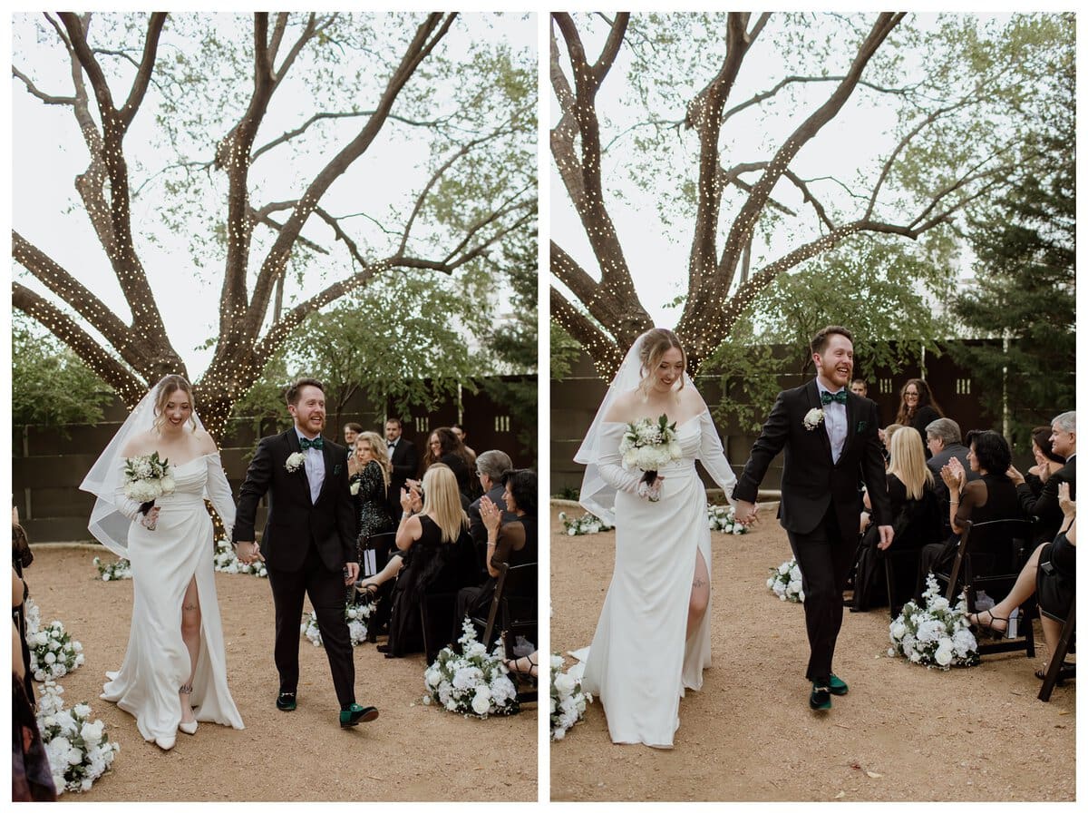 A newlywed couple joyfully walks down the aisle after saying "I do" at their Artspace111 Fort Worth wedding. The bride, in an elegant off-the-shoulder gown with a thigh-high slit, holds a bouquet of white flowers, while the groom, dressed in a black tuxedo with a green bow tie, smiles brightly.