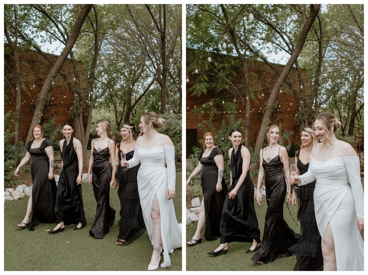 A joyful bride in an elegant off-the-shoulder white gown walks with her bridesmaids in matching black dresses at Artspace111 Fort Worth wedding venue. The lush outdoor garden setting, string lights, and brick backdrop create a sophisticated yet relaxed atmosphere, perfect for a modern wedding celebration.