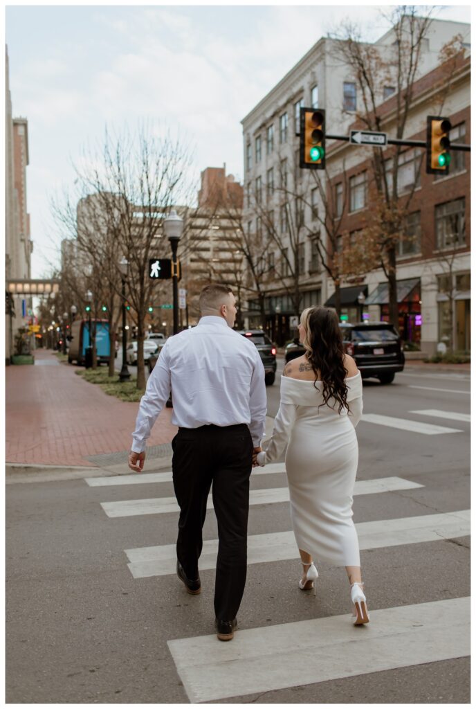 Engaged couple holding hands while walking across a crosswalk in downtown Fort Worth during their engagement photo session.