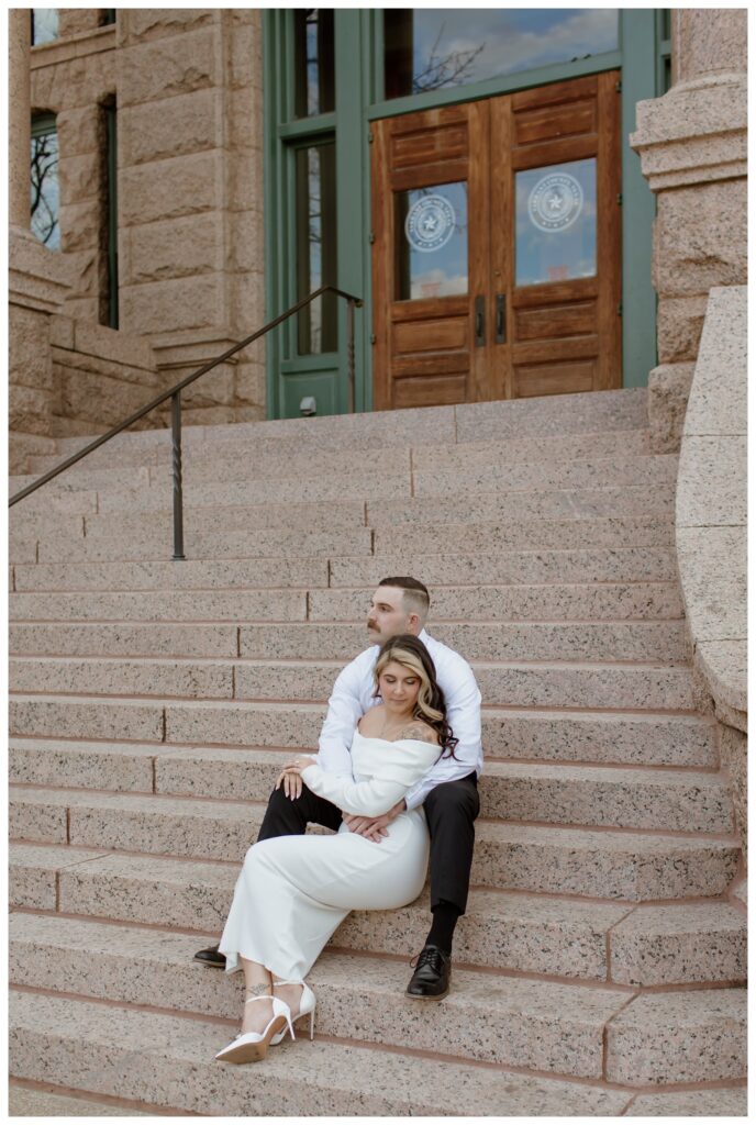 Engaged couple sitting on the grand stone steps of the Tarrant County Courthouse in downtown Fort Worth, sharing a romantic moment.