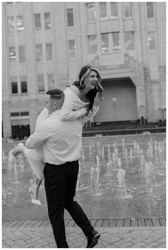 Playful engagement session in downtown Fort Worth's Sundance Square, featuring a couple laughing near the iconic fountains.