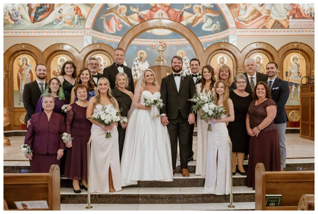 An extended wedding family photo with adults dressed in formal attire in a church, captured by a Fort Worth wedding photographer.
